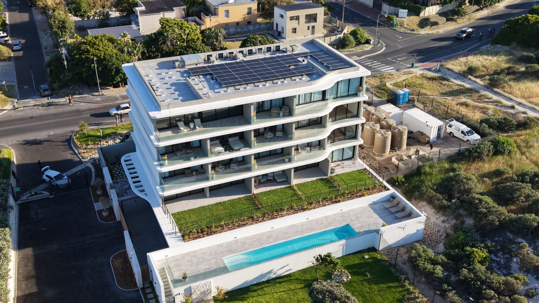 Drone photo of a beachfront building with curved white balconies, a lap pool terrace and the solar array on its roof