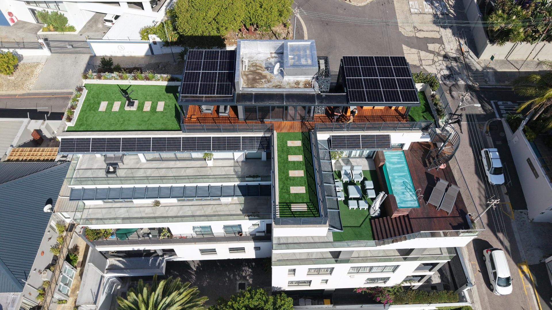 Top-down drone photo showing solar panels arranged around the rooftop terraces, pool and green roof of a Sea Point penthouse