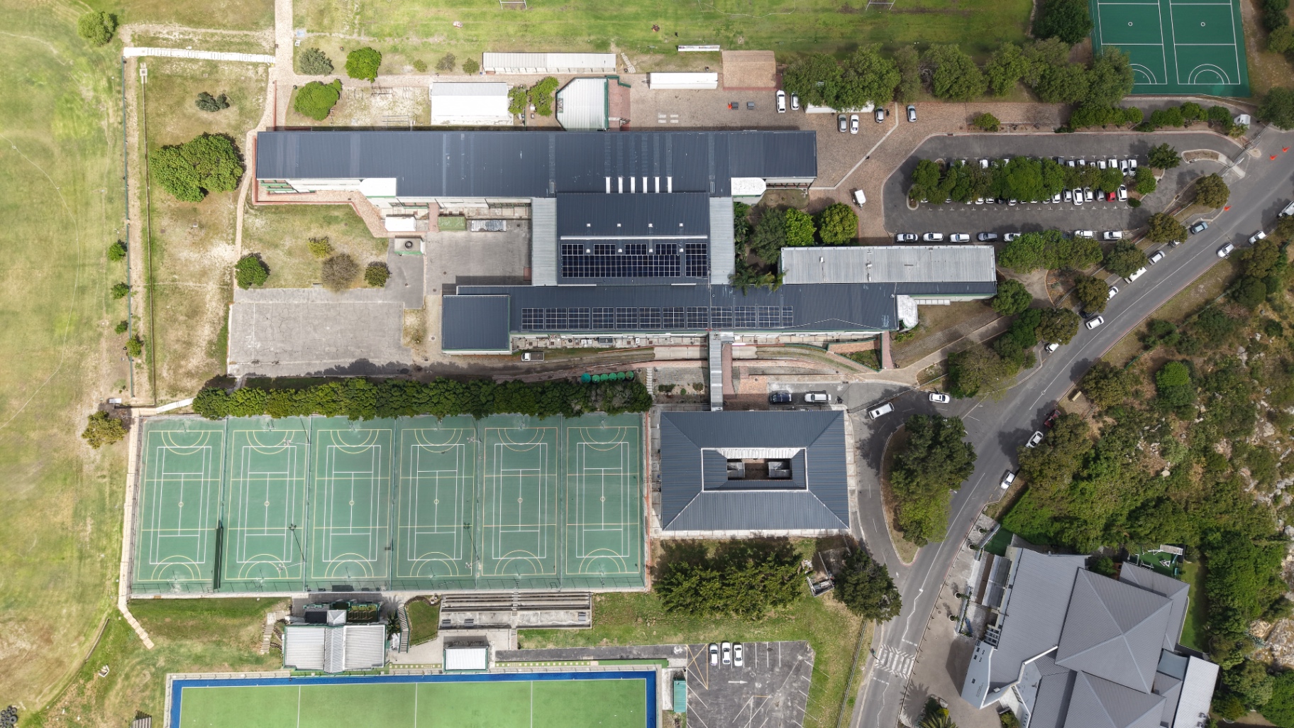 Top-down drone view of Tygerberg Hoërskool with solar arrays across the hall and classroom block roofs, sports fields around it