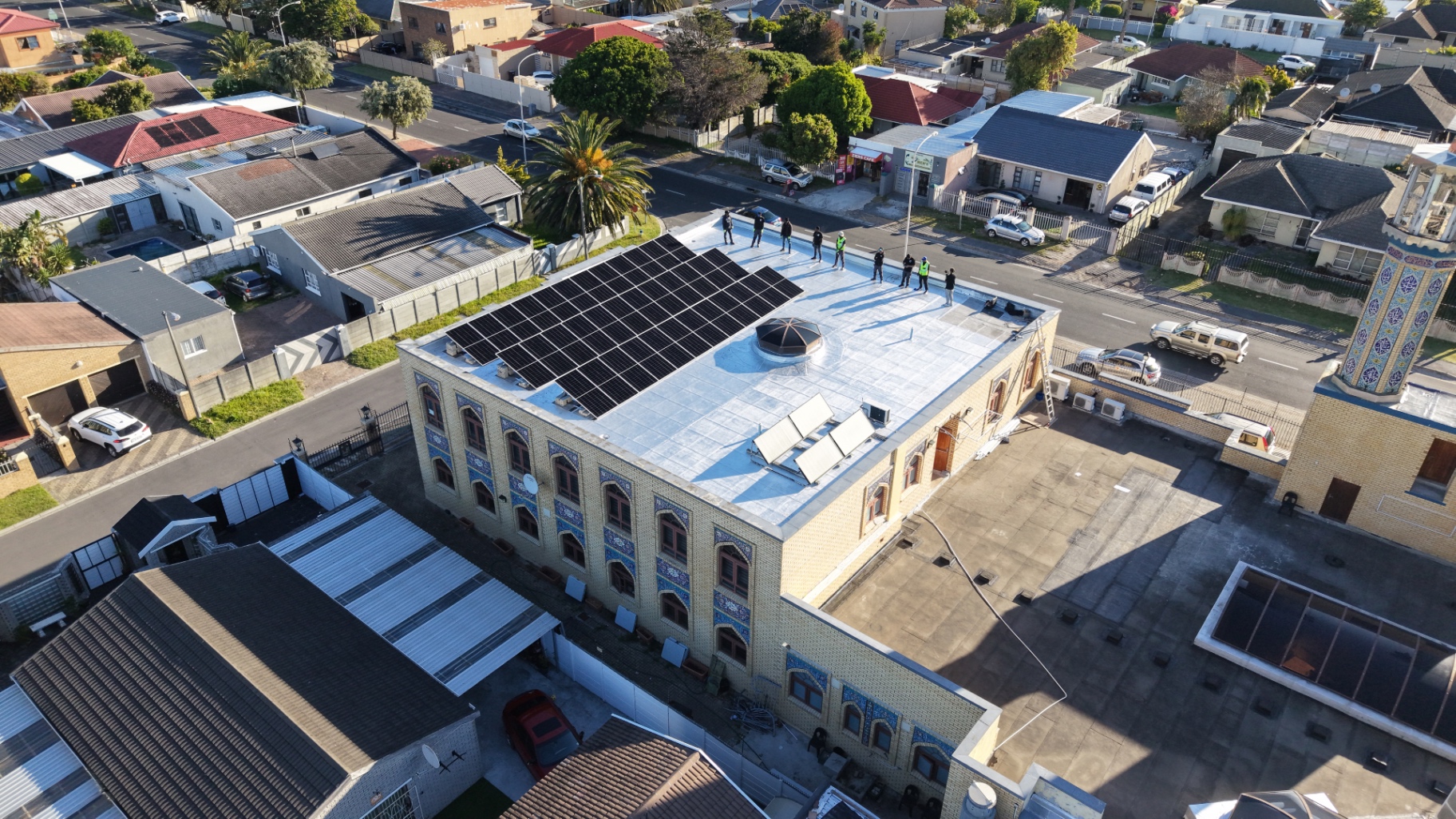 Drone view of the Ahlul Bait Mosque in Ottery with rows of solar panels across its flat roof and its blue-tiled minaret
