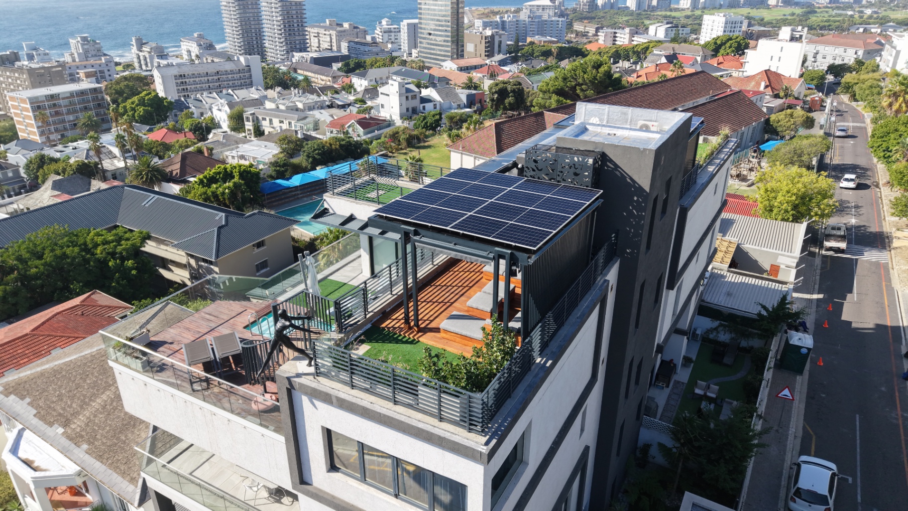 Drone view of a Sea Point penthouse with a custom solar array over its rooftop entertainment deck, the sea and promenade behind